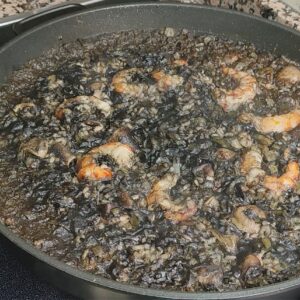 Arroz negro con marisco cocinado en sartén, con gambas y tinta de calamar sobre fuego