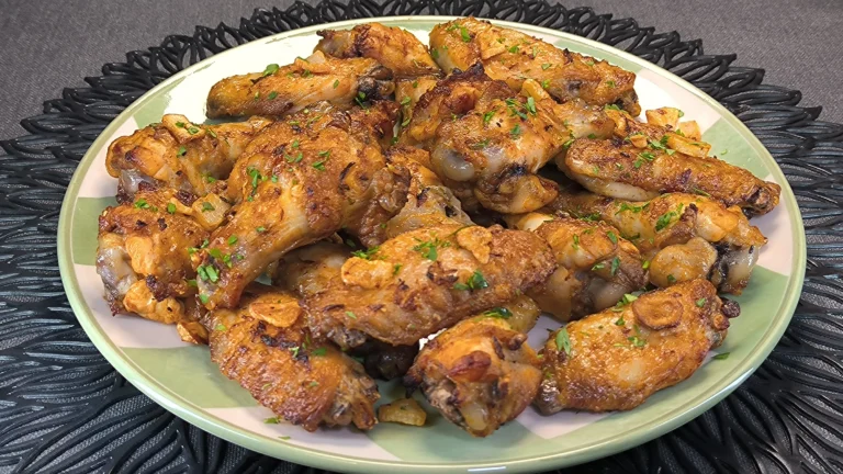 Alitas de pollo doradas y crujientes con ajos laminados y perejil fresco servidas en un plato blanco.