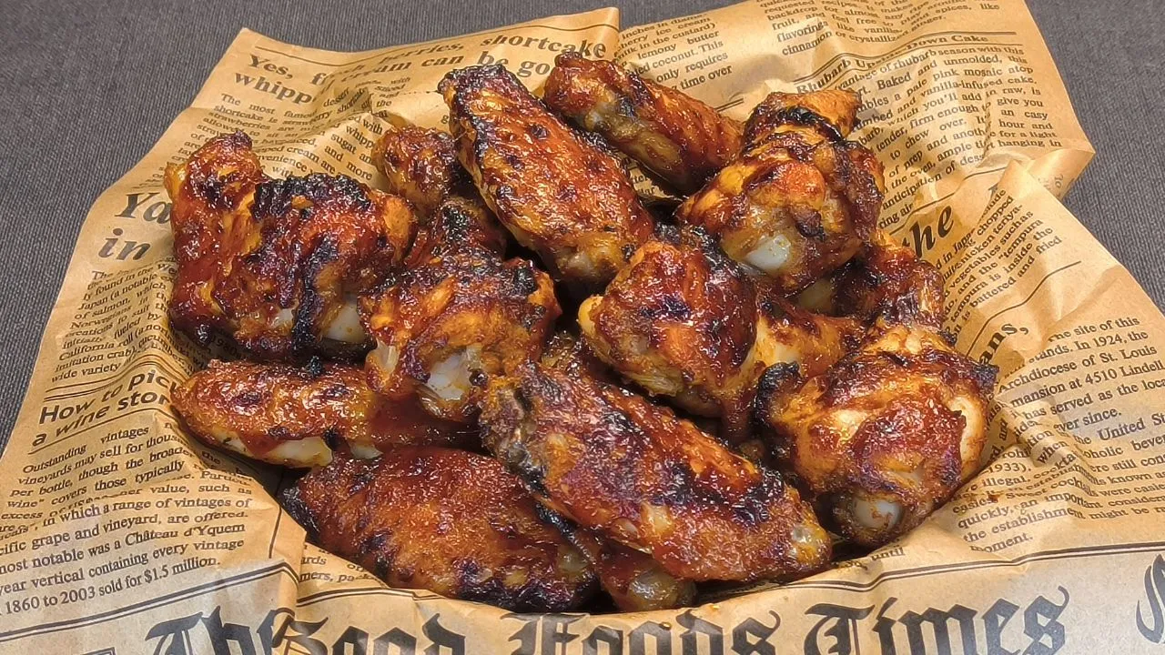 Alitas de pollo glaseadas con salsa barbacoa brillante y sésamo espolvoreado dentro de la cesta de una freidora de aire.