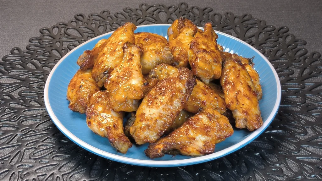 Alitas de pollo crujientes glaseadas con salsa de mostaza y miel servidas en un plato oscuro con guarnición de brotes verdes.