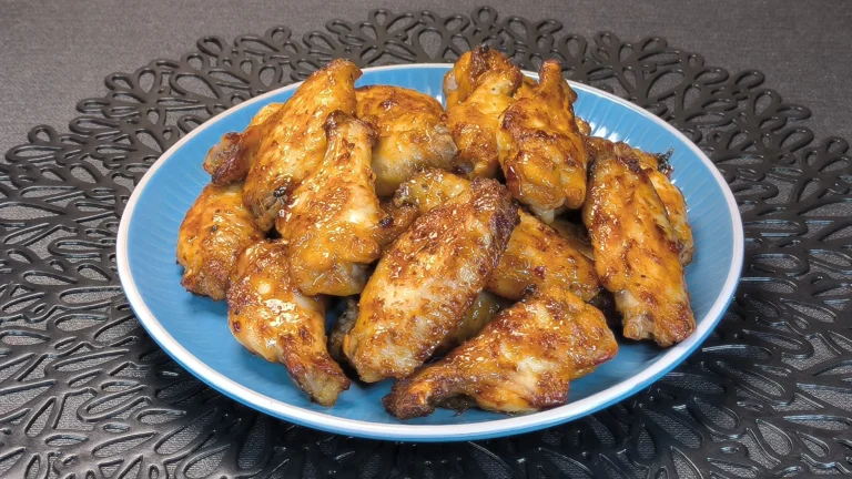 Alitas de pollo crujientes glaseadas con salsa de mostaza y miel servidas en un plato oscuro con guarnición de brotes verdes.