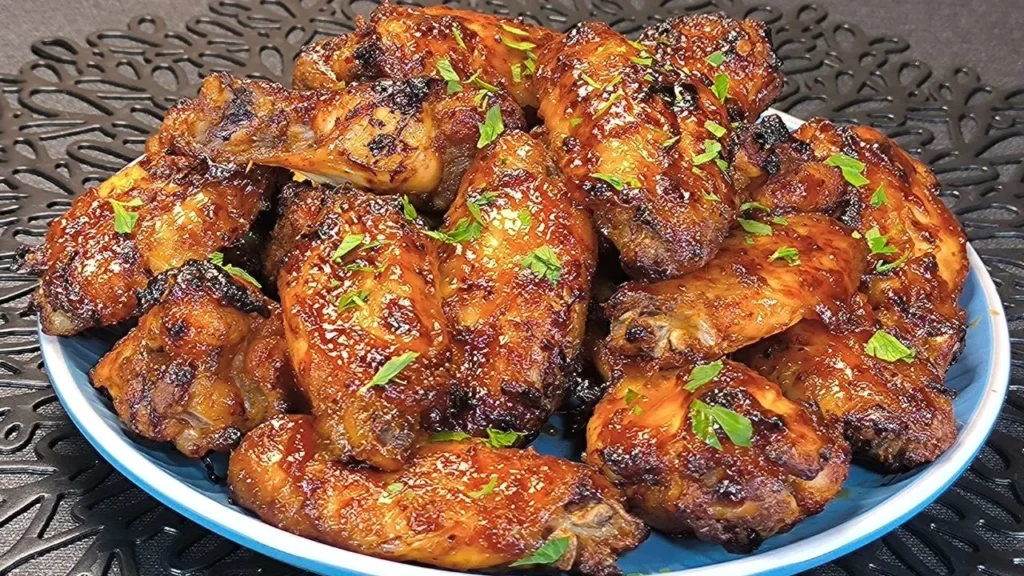 Alitas de pollo doradas bañadas en salsa agridulce roja con semillas de sésamo y cebollino picado en un plato blanco.