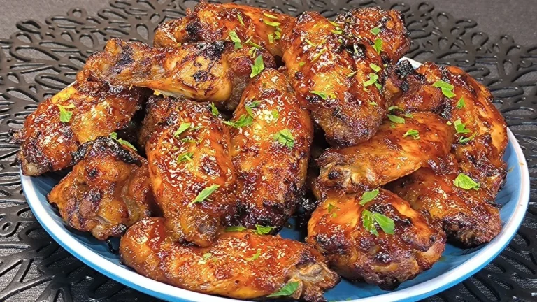 Alitas de pollo doradas bañadas en salsa agridulce roja con semillas de sésamo y cebollino picado en un plato blanco.