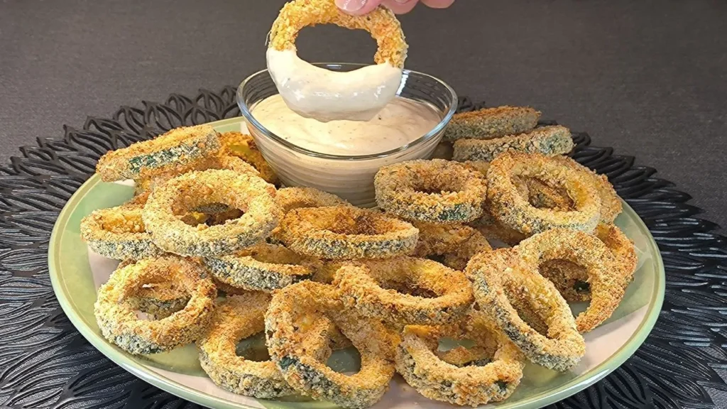 Aros de calabacín crujientes rebozados y dorados en freidora de aire servidos con salsa cremosa