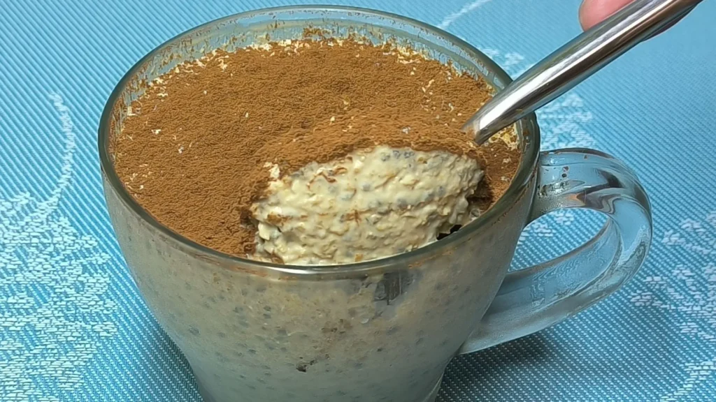 Avena Café: Desayuno Saludable y Energético en 2 Minutos 1 Vaso de cristal con capas de avena hidratada en café, yogur griego y cacao en polvo espolvoreado por encima.
