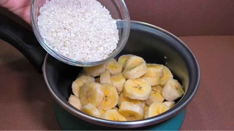 Vaso de cristal con bebida de plátano y arroz cremosa acompañado de rodajas de plátano fresco y una pajita decorativa.