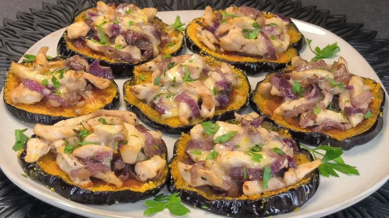 Rodajas de berenjena cubiertas con pollo y un rebozado dorado de copos de maíz crujientes, servidas con aros de cebolla roja.