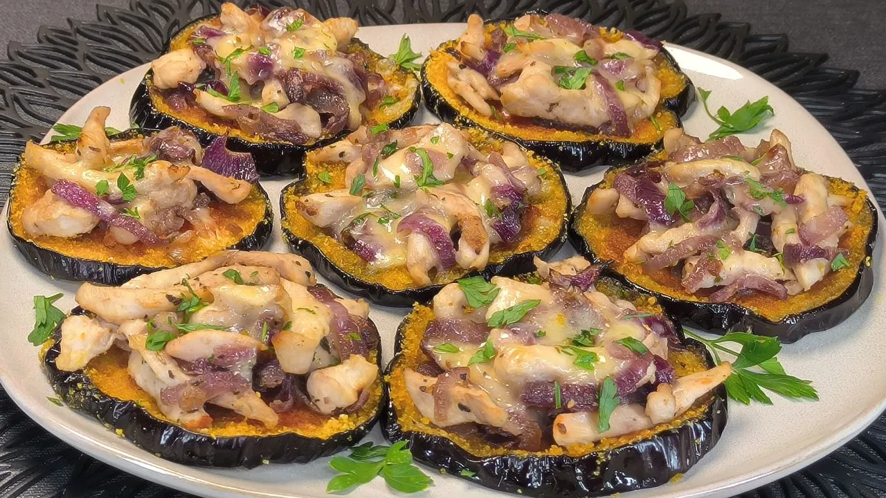 Rodajas de berenjena rellena de pollo y queso y un rebozado dorado de copos de maíz crujientes, servidas con aros de cebolla roja.