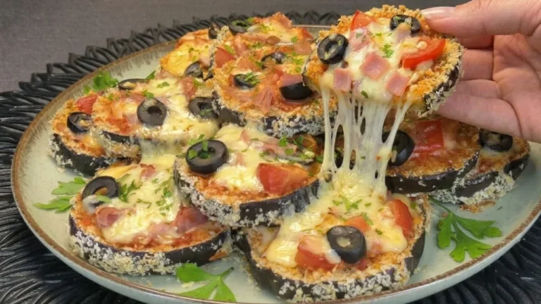 Rodajas de berenjena rebozadas en pan rallado panko crujiente, horneadas y cubiertas con salsa de tomate, queso fundido y especias sobre una bandeja con papel vegetal.