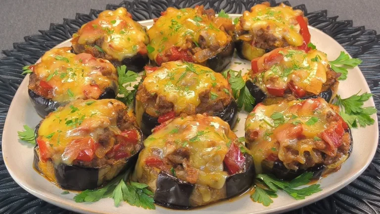 Berenjenas asadas rellenas de carne picada y pimiento rojo picadito, servidas en una fuente blanca sobre un mantel individual de mimbre.