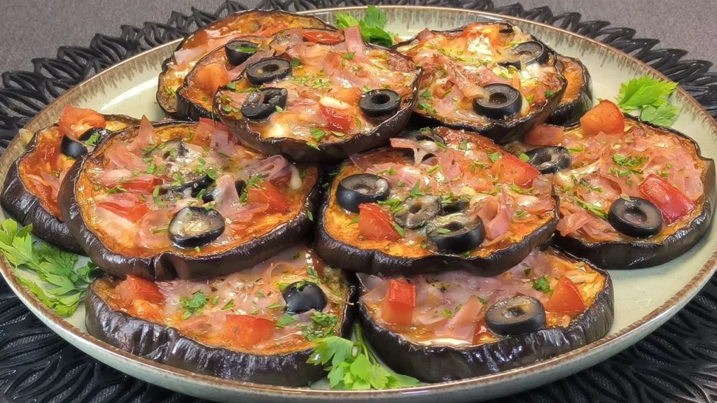 Rodajas de berenjena asadas cubiertas con salsa de tomate, queso fundido y especias sobre una bandeja de horno.