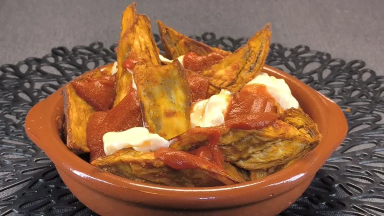 Berenjenas cortadas en dados, fritas y servidas con salsa brava casera y alioli sobre un plato blanco.