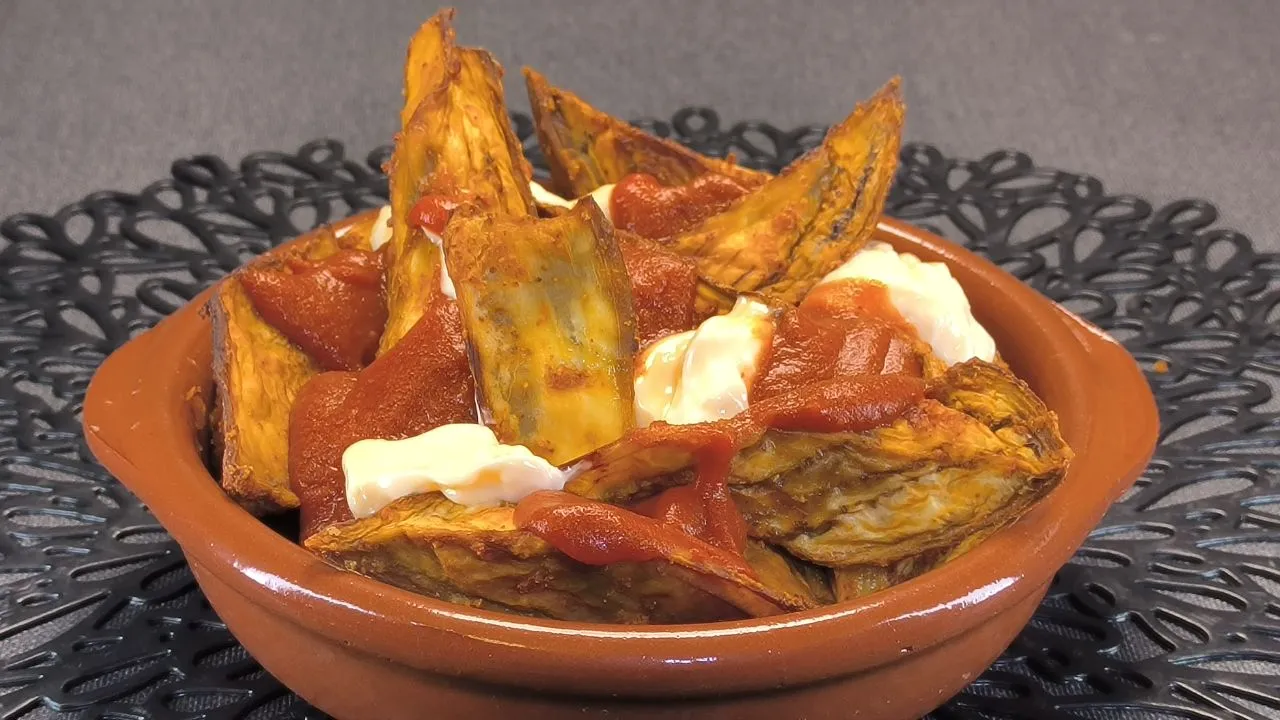 Berenjenas cortadas en dados, fritas y servidas con salsa brava casera y alioli sobre un plato blanco.