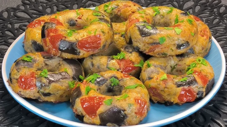 Seis donuts de berenjena rebozados y dorados con queso fundido por encima colocados en la rejilla de una freidora de aire.