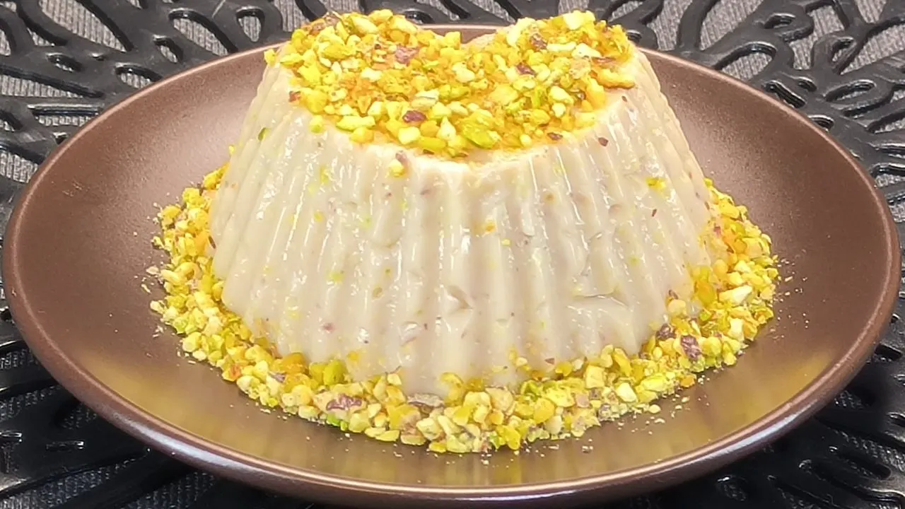 Dos flanes de pistacho desmoldados sobre platos blancos, elaborados con bebida de avena y decorados con pistachos troceados.