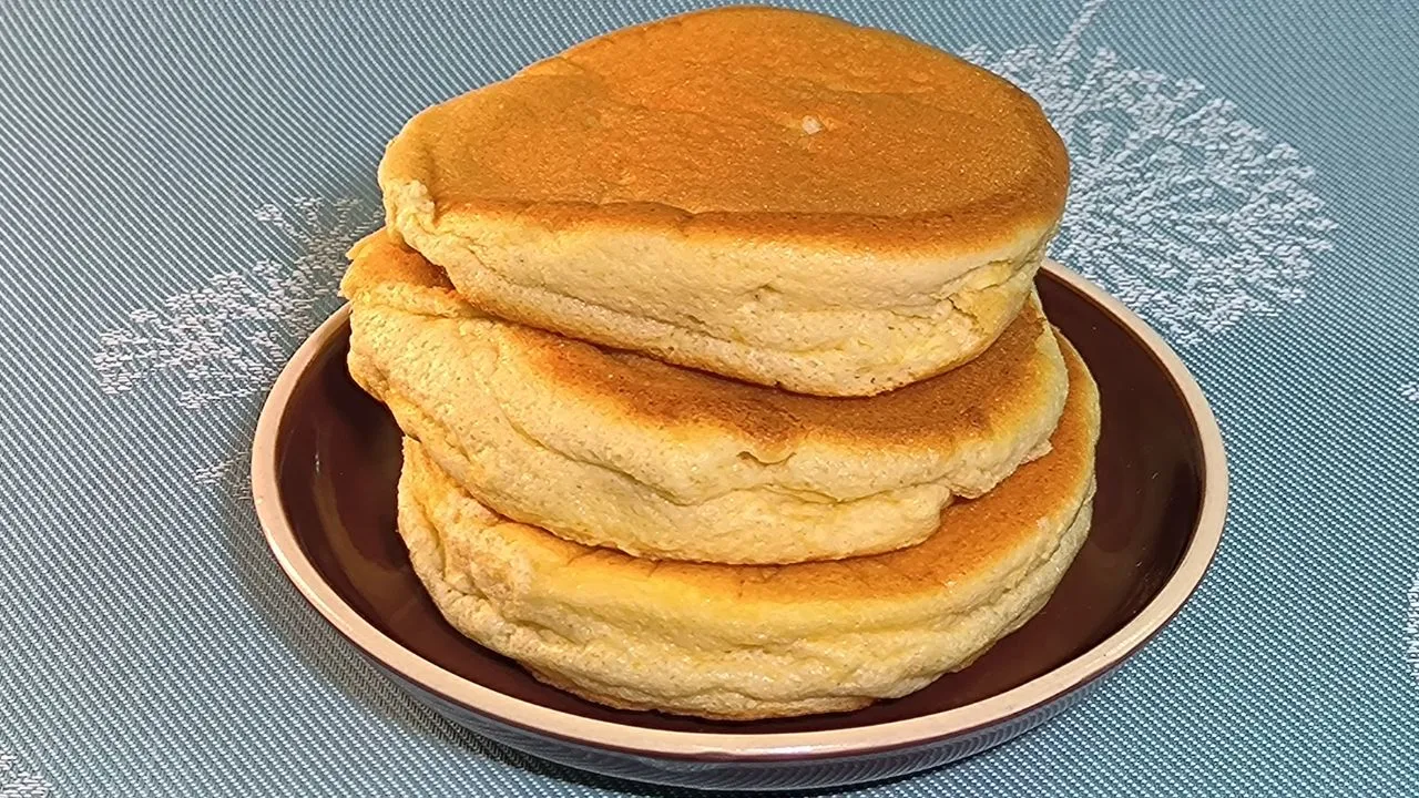 Torre de fluffy pancakes americanos esponjosos decorados con mantequilla y jarabe de arce sobre un plato blanco.