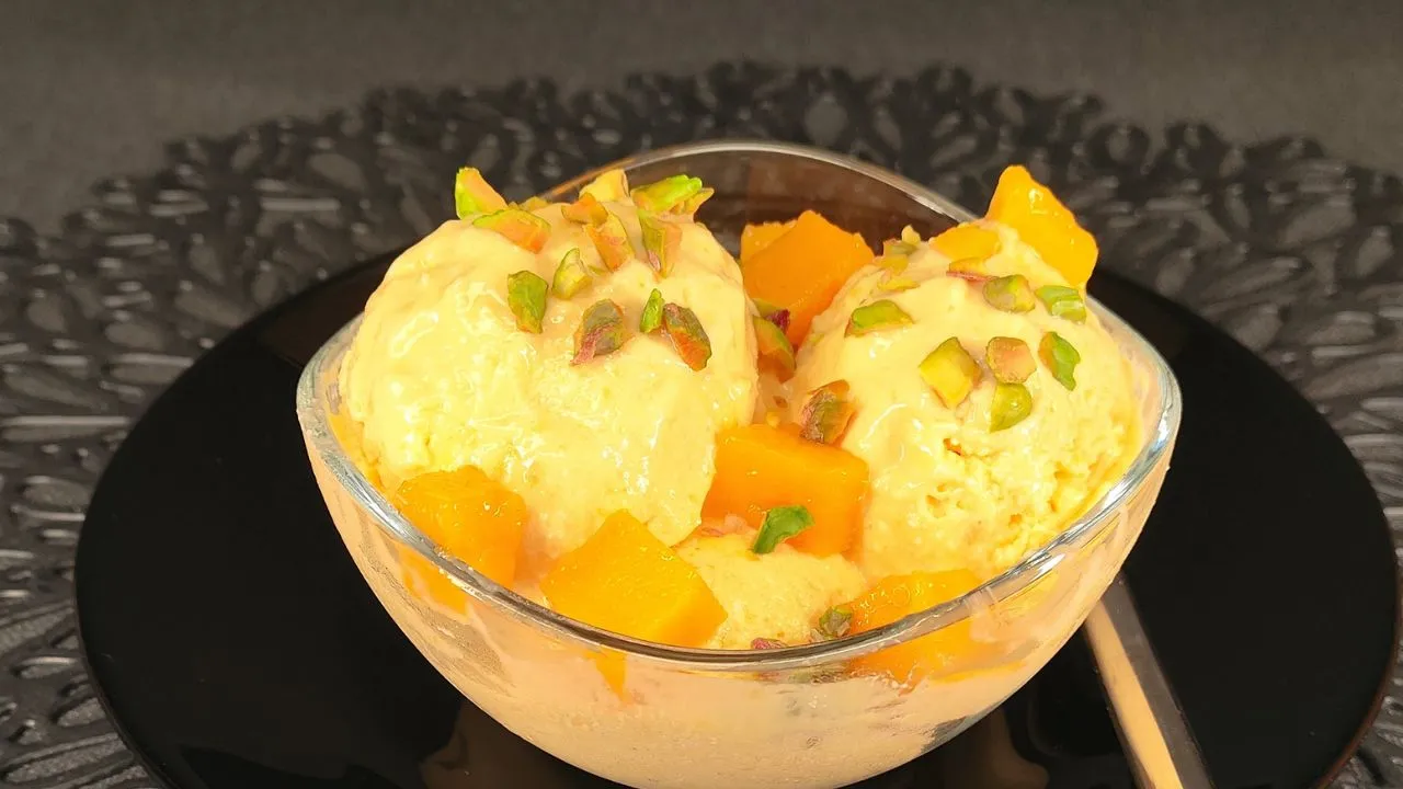 Helado de mango saludable elaborado con queso cottage cremoso, servido en un bol de cristal y decorado con trozos de mango fresco y hojas de menta sobre un fondo luminoso.