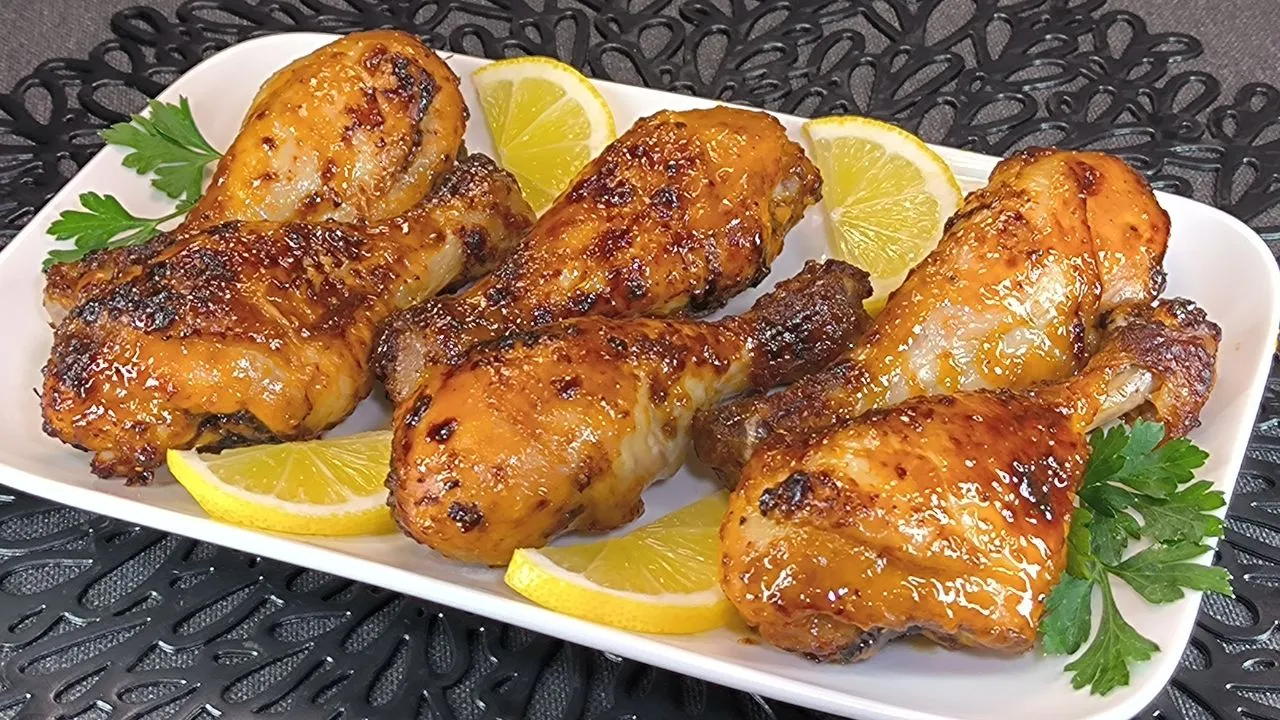 Tres muslos de pollo glaseados con salsa de miel y mostaza dorados en freidora de aire, servidos en un plato oscuro con guarnición de patatas fritas.