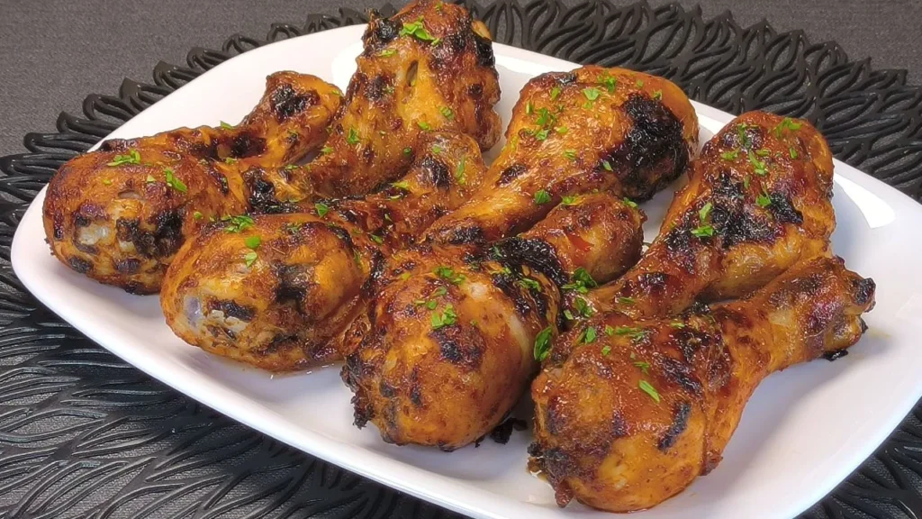 Tres muslos de pollo dorados bañados en salsa agridulce con semillas de sésamo y cebollino, servidos en un plato blanco tras cocinarse en freidora de aire.