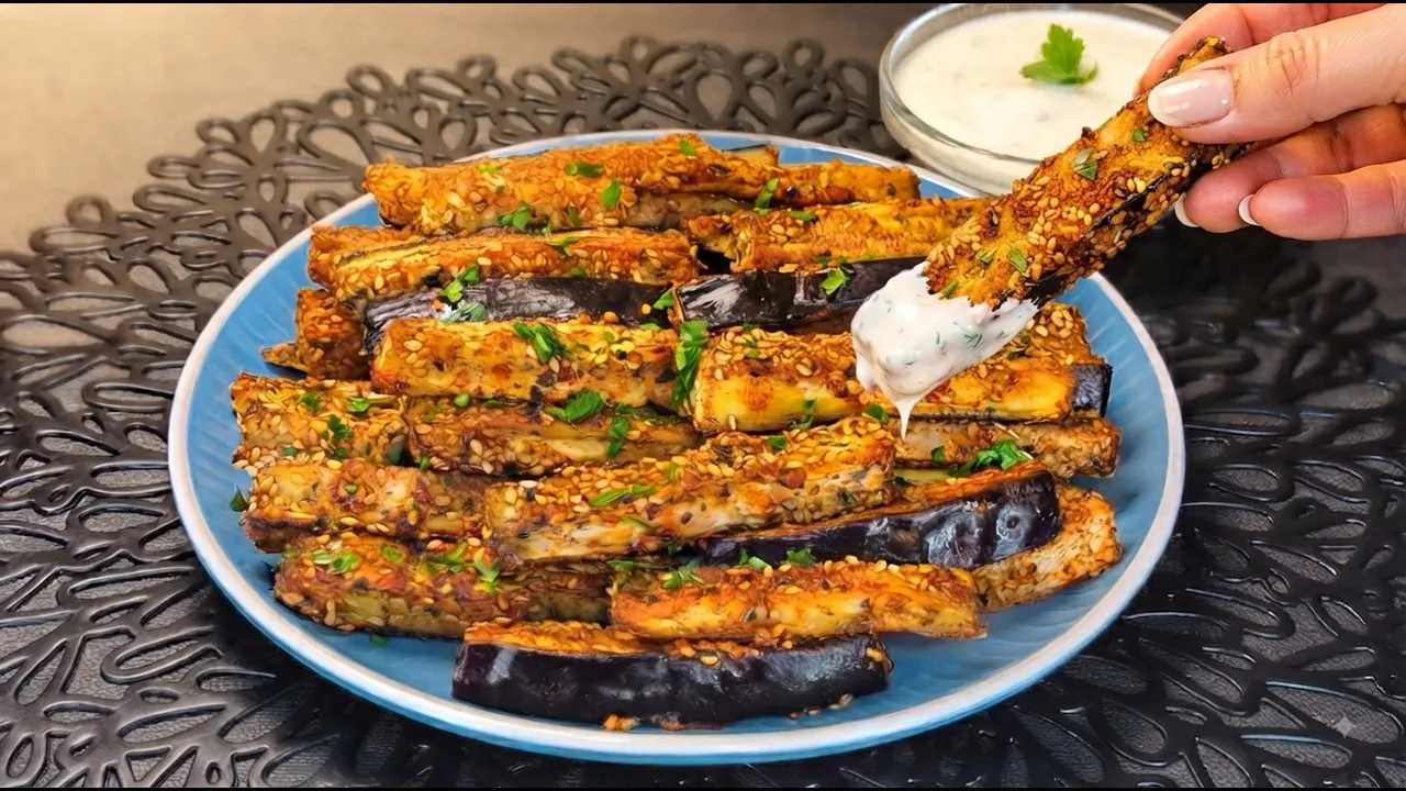 Palitos de berenjena al horno crujientes rebozados en semillas de sésamo doradas, presentados en un cuenco junto a una salsa para mojar.