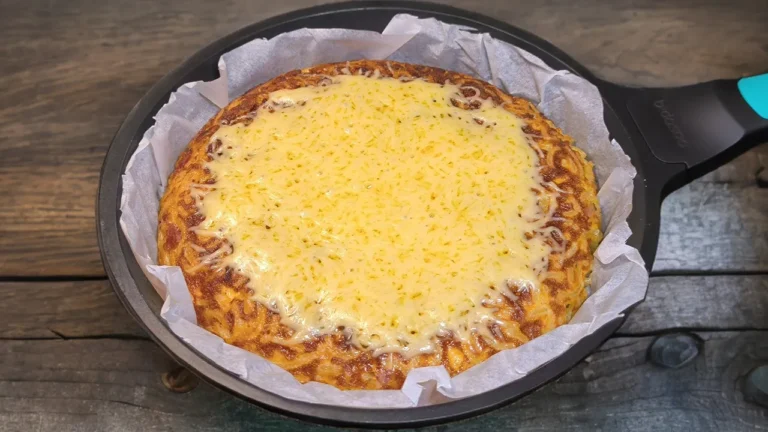 Pastel de pasta dorado en sartén con trozos de bacon crujiente, queso fundido y una textura gratinada.