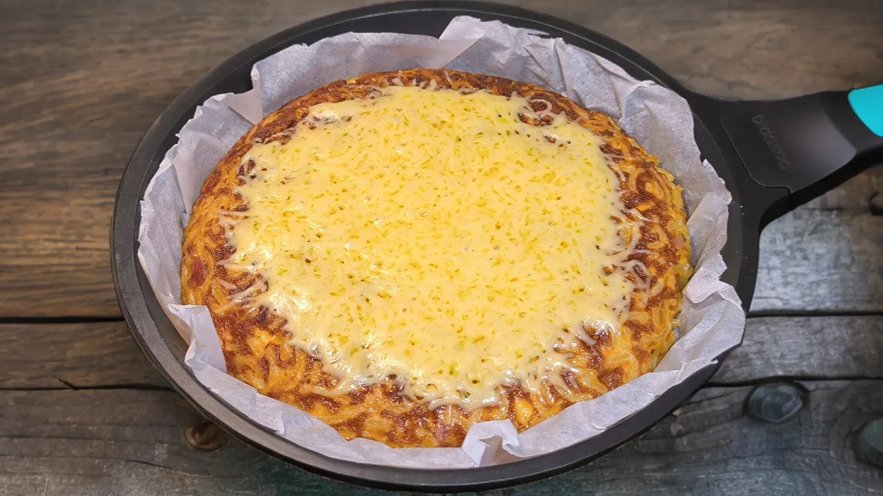 Pastel de pasta dorado en sartén con trozos de bacon crujiente, queso fundido y una textura gratinada.