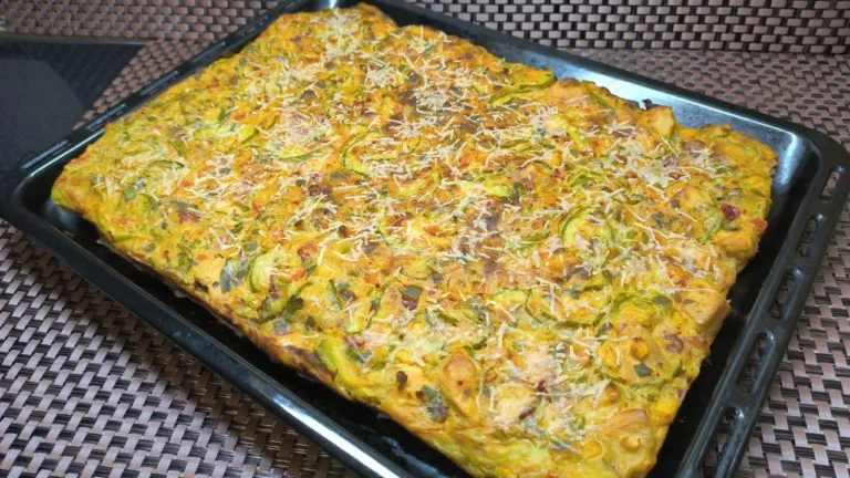 Pastel de verduras y pechuga de pollo desmenuzada con cobertura de queso fundido, servido en una bandeja de horno blanca.