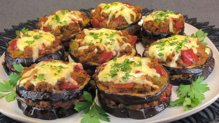 Dos rodajas de pasteles de berenjena rellenos con carne picada y gratinados, servidos en un plato blanco con decoración de perejil.