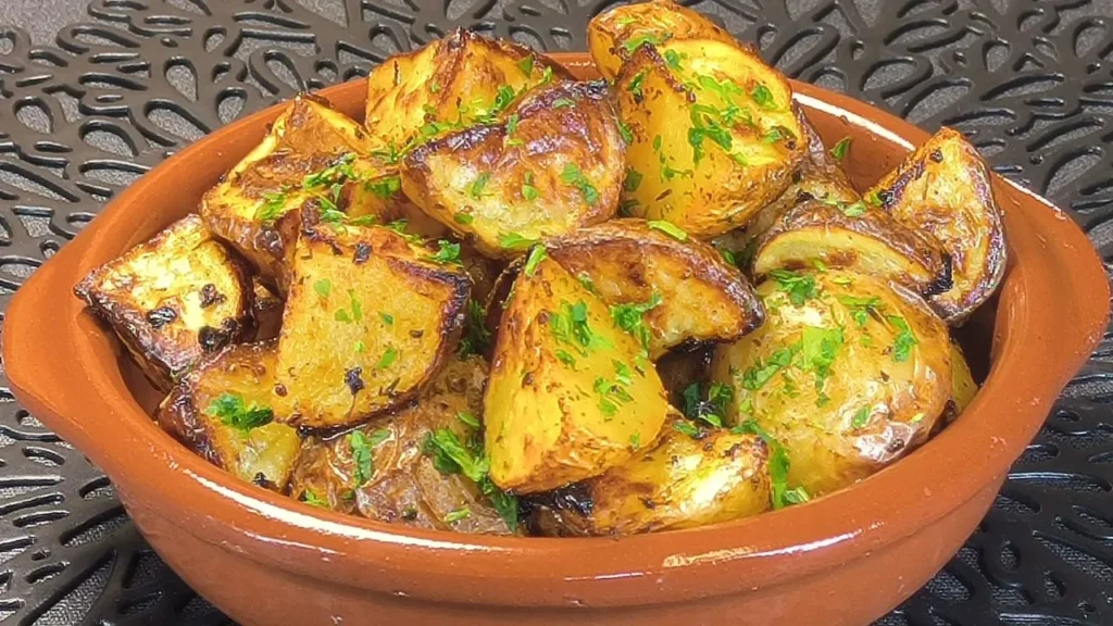 Patatas gajo doradas y crujientes sazonadas con perejil fresco, ajo y rodajas de limón, servidas en un plato blanco hondo sobre una mesa de madera.