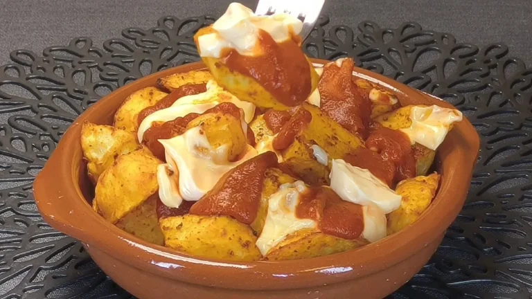 Patatas bravas crujientes hechas en freidora de aire con salsa brava casera y perejil en un cuenco blanco.