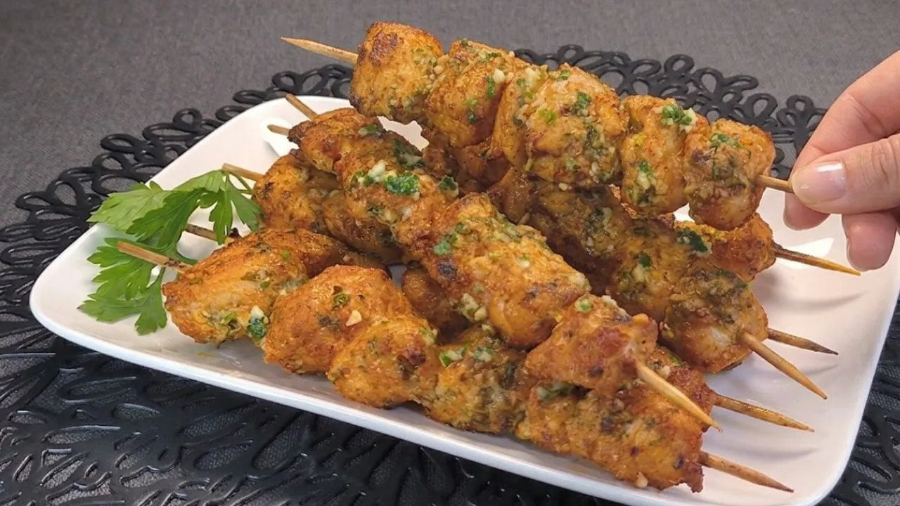 Cuatro brochetas de pechuga de pollo marinadas con ajo y queso parmesano rallado, perfectamente doradas y crujientes sobre la rejilla de una freidora de aire abierta.