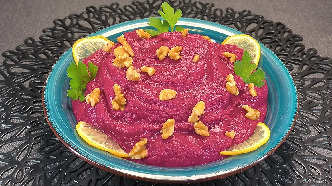 Bol de hummus de judías blancas con remolacha de color rosado brillante, servido en una mesa de cocina rústica