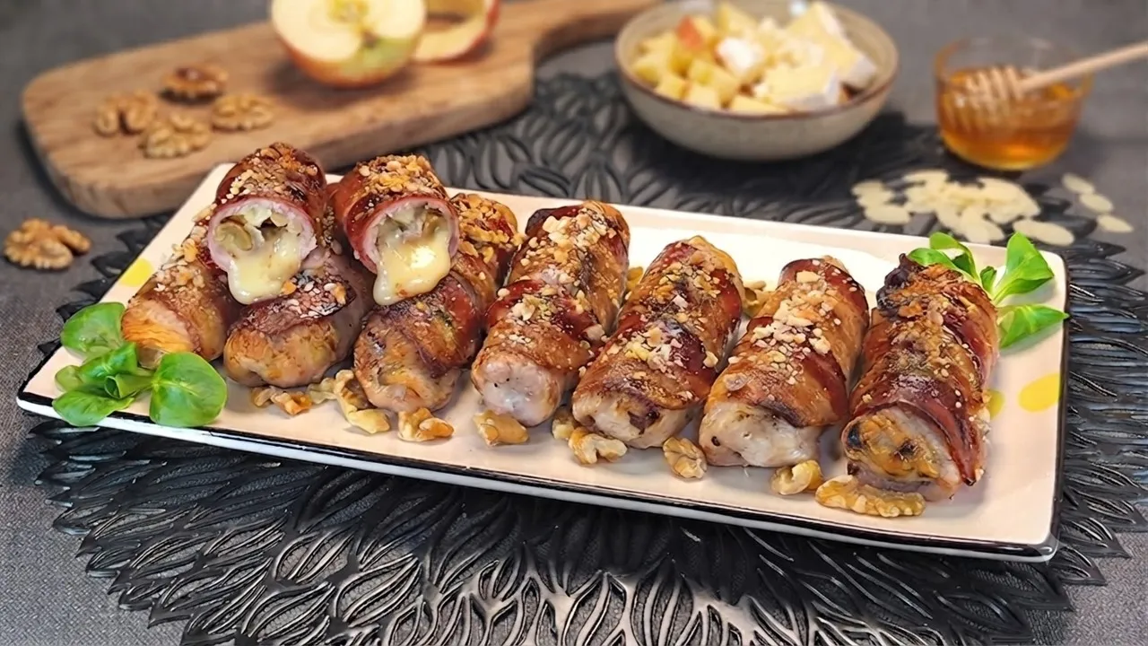 Rollitos de pollo con bacon y queso brie: 3 trucos para un resultado crujiente 1 Rollitos de pollo con bacon y queso brie rellenos de manzana, nueces y queso brie fundido, servidos en una fuente sobre tabla de madera.