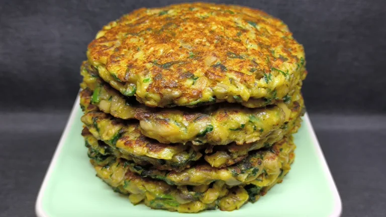 Tres tortitas de espinacas y champiñones doradas servidas en un plato blanco con guarnición de brotes verdes y tomates cherry.