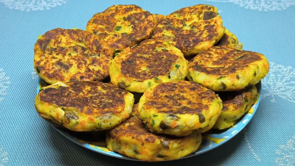 Tortitas doradas de patata rallada y champiñones picados apiladas sobre un plato blanco con un toque de perejil.