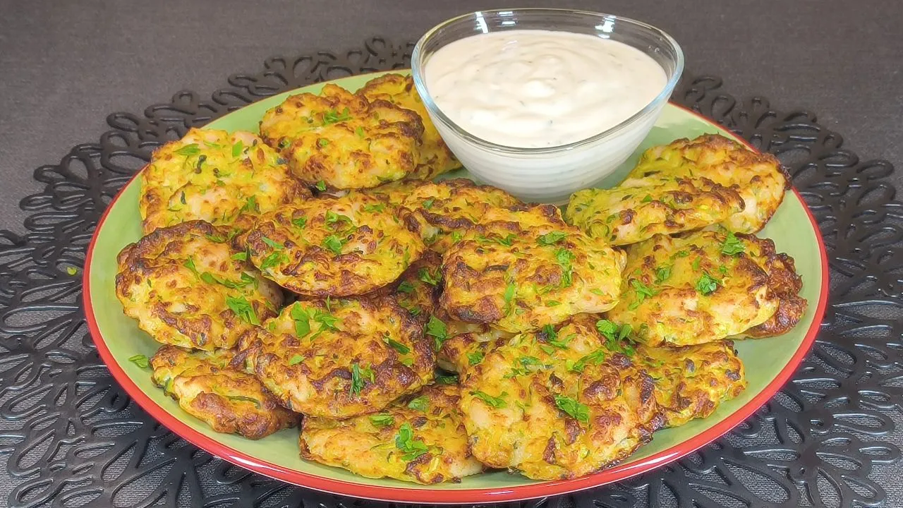 Tortitas doradas de pollo picado y calabacín rallado servidas en un plato blanco con una guarnición de ensalada fresca de canónigos y tomates cherry.