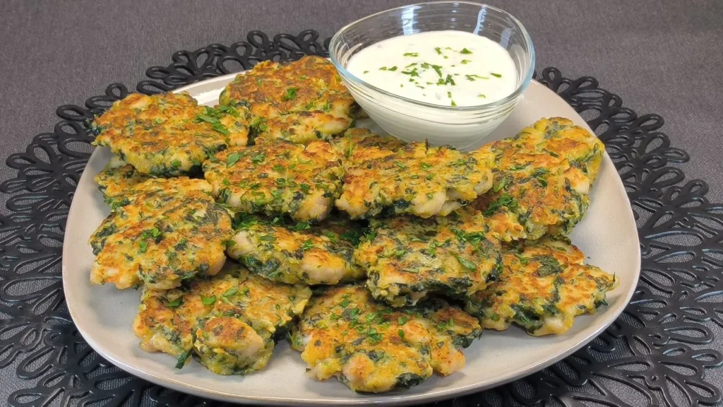 Tres tortitas de pollo con espinacas picadas dorándose en una sartén negra sobre una encimera de cocina.