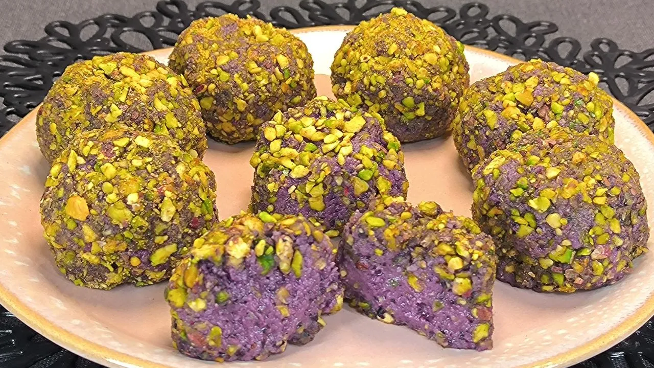 Trufas saludables de arándanos recubiertas con granillo de pistacho verde y almendra picada sobre una superficie de madera.